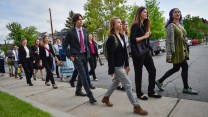 A group of youth of vary ages in business wear walk down a sidewalk.