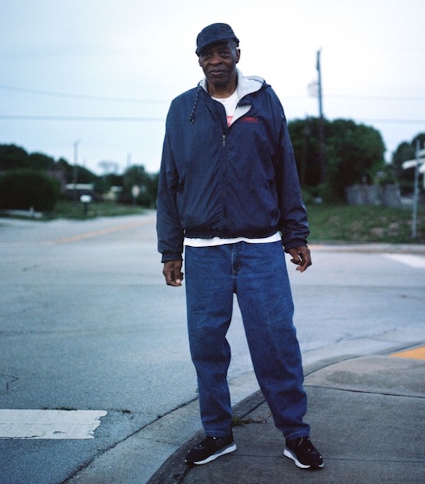 A Black man standing on a sidewalk in jeans and a jacket