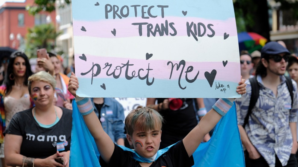 A child walking in a trans pride march holds up a sign saying "Protect trans kids, protect me."