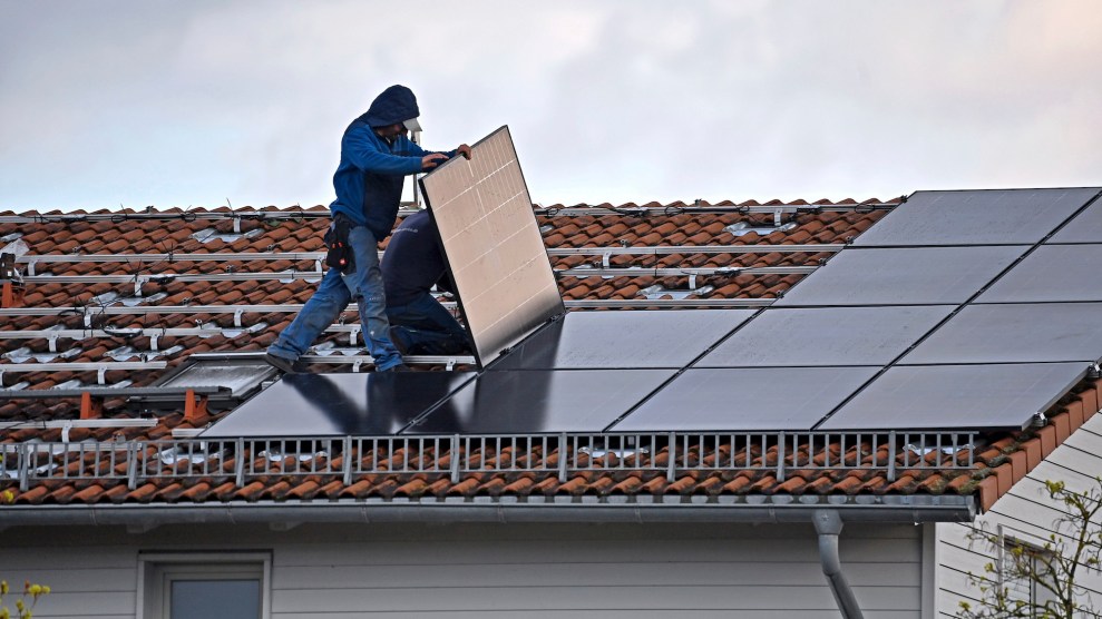 A worker wearing jeans and a jacket installing solar panels on a red house roof.