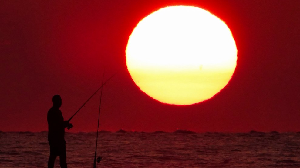 A fisherman silhouetted against a dramatic sunrise appearing as a giant ball over the beach, July 12, 2023 in Isle of Palms, South Carolina. The sky is red.