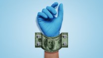 A hand wearing a blue surgical glove is shackled to a blue wall. The shackle is made of a 100 dollar bill and is attached with bolts.