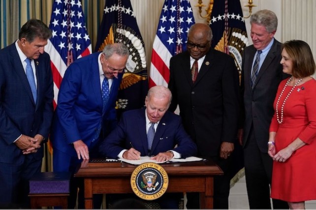 Biden signing a piece of paper with , Sen. Joe Manchin, D-W.Va., Senate Majority Leader Chuck Schumer of N.Y., House Majority Whip Rep. James Clyburn, D-S.C., Rep. Frank Pallone, D-N.J., and Rep. Kathy Castor, D-Fla., standing around him