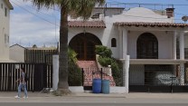 A person walking in front of a house in Baja, Mexico. A palm tree is visible