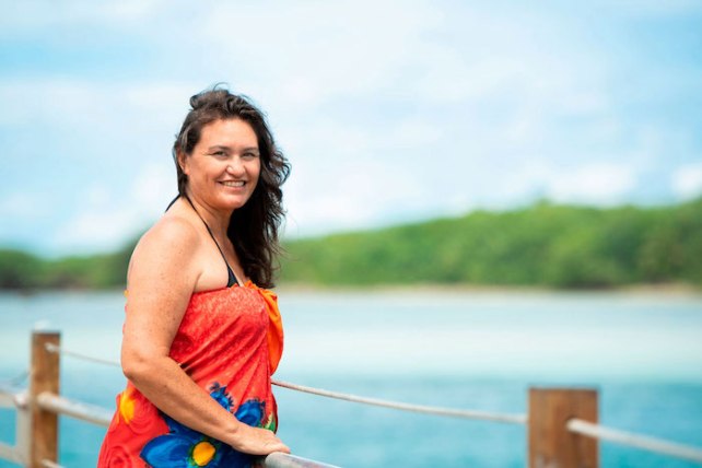 Jacqui Evans, a woman with black hair and light brown skin stands against a backdrop of the ocean.