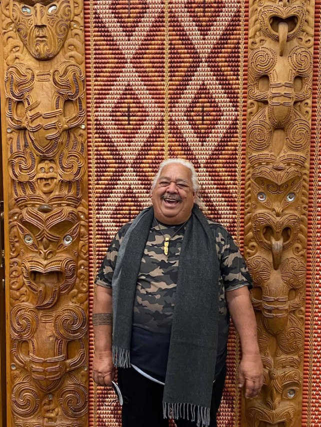 Michael Tavioni, a man with brown skin and white hair, smiling against a backdrop of artwork
