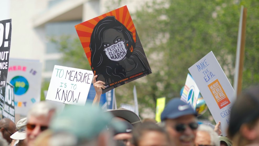A protest on climate change, with a few signs visible, the largest is one with a Black woman on it wearing a white mask that says "People's Climate March"