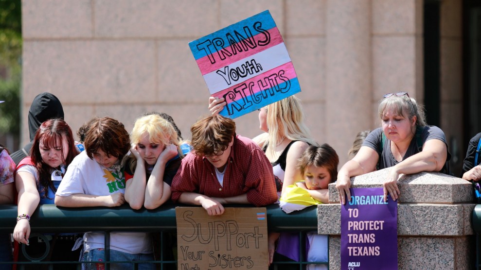 I manifestanti si riposano sul balcone del terzo livello della rotonda esterna dell'edificio di estensione del Campidoglio del Texas per osservare la protesta dall'alto.  Reggono cartelli a sostegno dei giovani transgender.