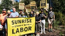 A group of people, mostly masked, hold yellow and black signs with slogans like "Our future is non negotiable" and "Pass a bold civilian climate corps." In front of them several hold a banner that says "Sunrise stands with labor."