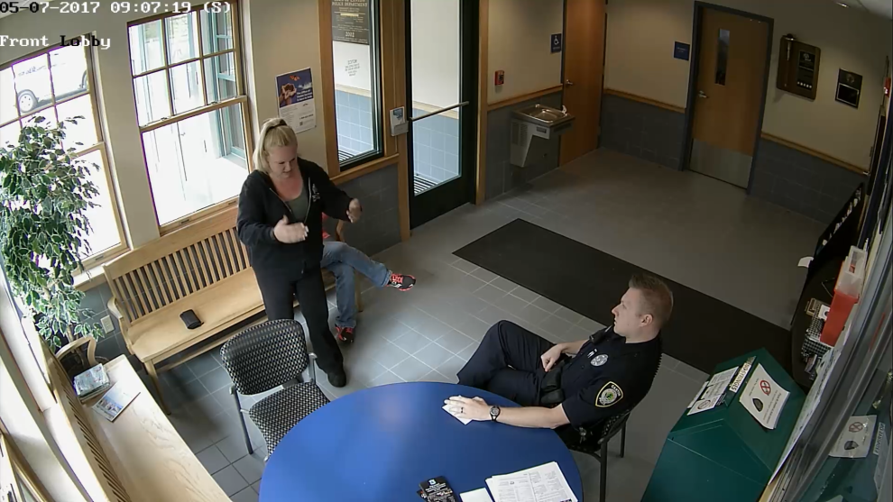 Adam Gompper sits at a table facing the building’s front door. Nicole Chase stands facing him.