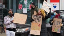 Workers hold protest signs outside of a Starbucks in support of unionization.