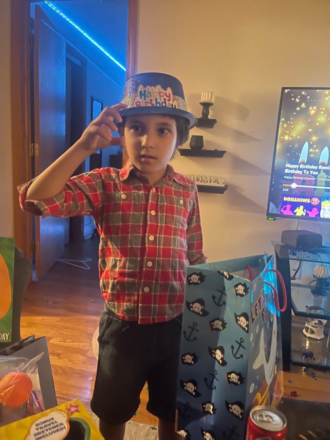 A six year old child wearing a birthday hat and a button up shirt.