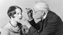 A male eye doctor shines a light into the eyes of a female patient