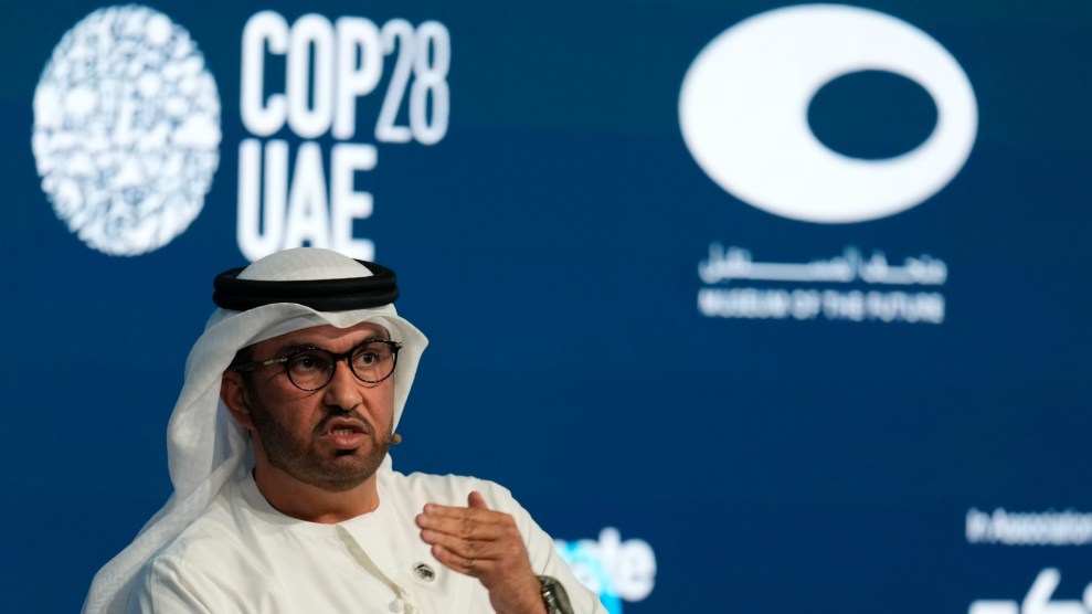 A Middle Eastern man wears a white thawb and speaks in front of a sign that says Cop28 UAE.