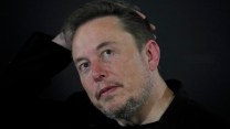Elon Musk in a black shirt putting a hand on his head