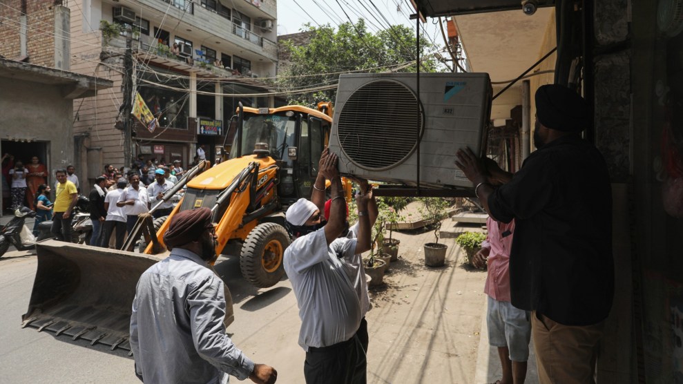 Two individuals hold a large air conditioner over their heads. Behind them, a bulldozer stands at the ready.