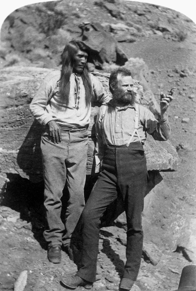 Explorer John Wesley Powell stands with a Native American man somewhere in the southwestern United States. 