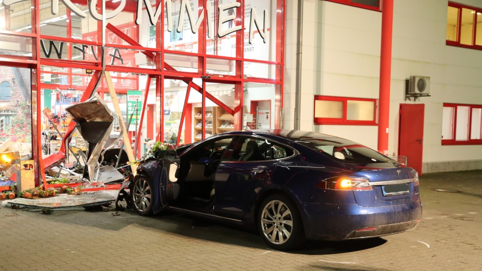 A Tesla stands after an accident in front of the destroyed entrance of a hardware store.