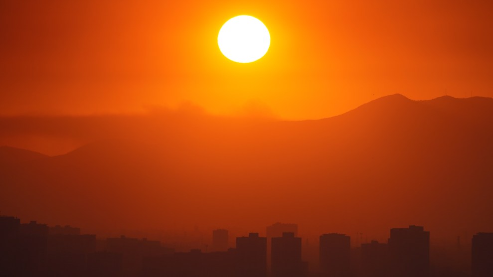The sky is orange, with a bright yellow sun, and buildings covered in smoke