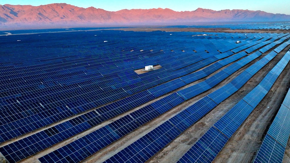 A huge valley is filled with dark blue solar panels. Pale red mountains surround it.