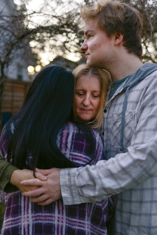 Woman with eyes closed hugging her two children, a girl with her head turned and teenage boy.