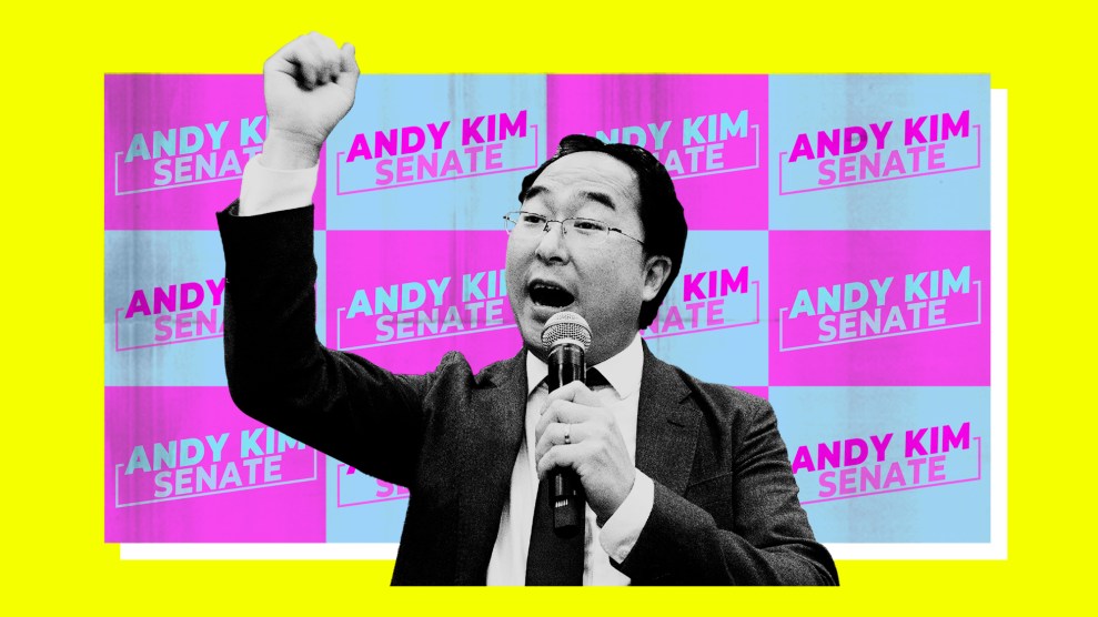 U.S. Representative Andy Kim, a Democrat running for Senate in New Jersey, pictured in black and white giving a speech with his right fist raised. He's set against a backdrop of light blue and magenta campaign signs that read 'Andy Kim: Senate'