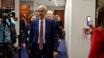 John Podesta walking in a White House hallway with people taking photos of him