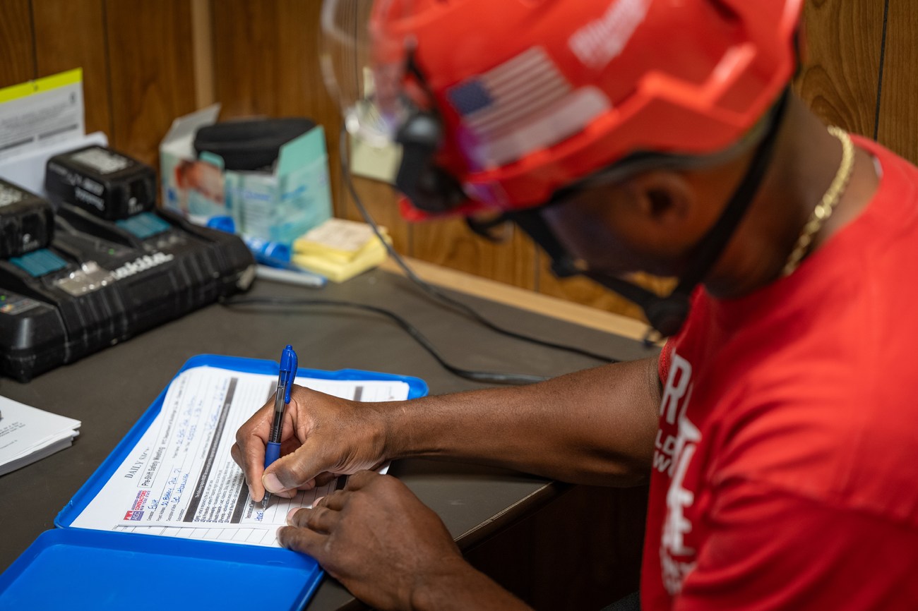 A man in a red hard hat signs papers.