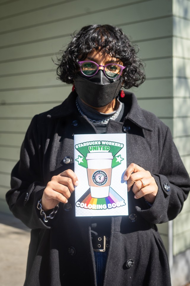 Portrait of a person in glasses holding a Starbucks Workers United coloring book.