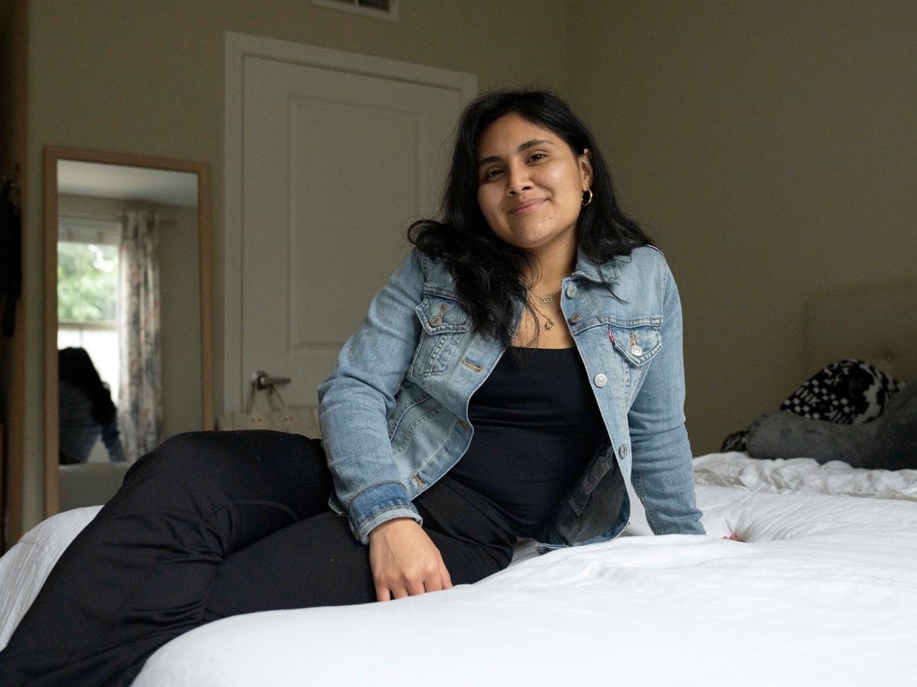 Woman sitting on bed, smiling at camera.