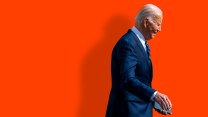 President Joe Biden walks to the right of the frame against a red background.