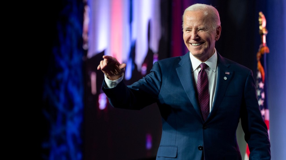 Joe Biden in a blue suit on a stage pointing ahead and smiling