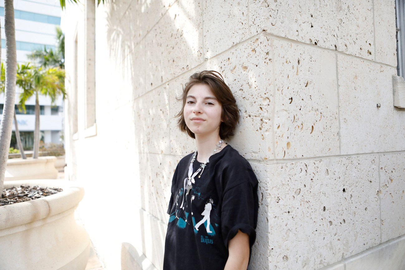 Portrait of young person in a black t-shirt standing next to a building.