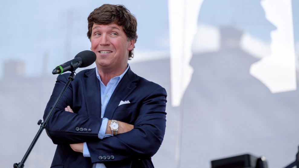 Conservative host Tucker Carlson stands in front of a microphone on a conference stage.
