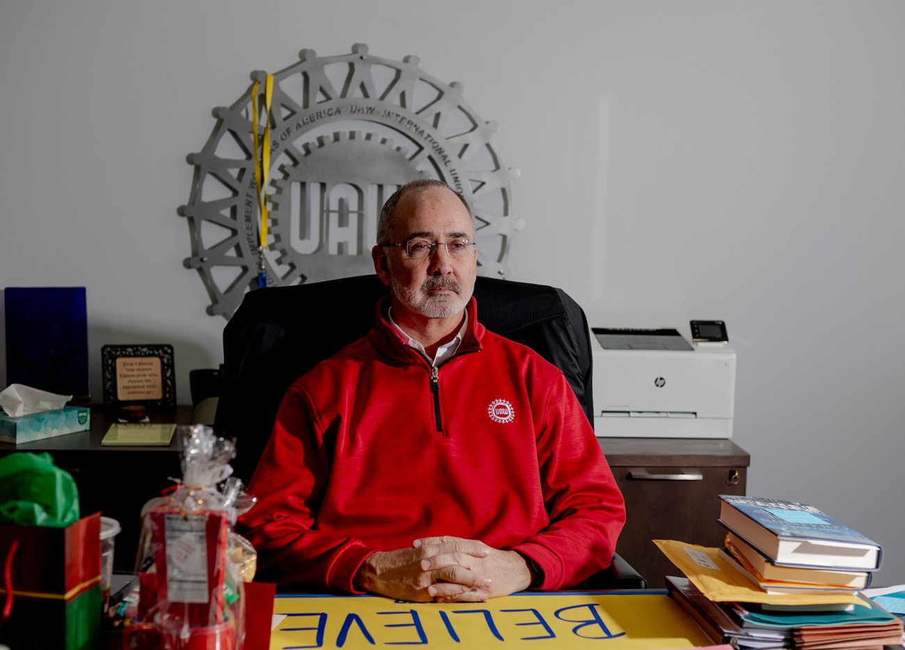 Shawn Fain, president of the UAW, sitting at a desk with the UAW logo beind him.