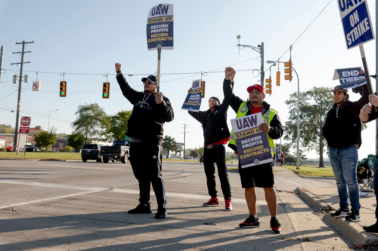 Group of people holding UAW strike signs, standing on the street.