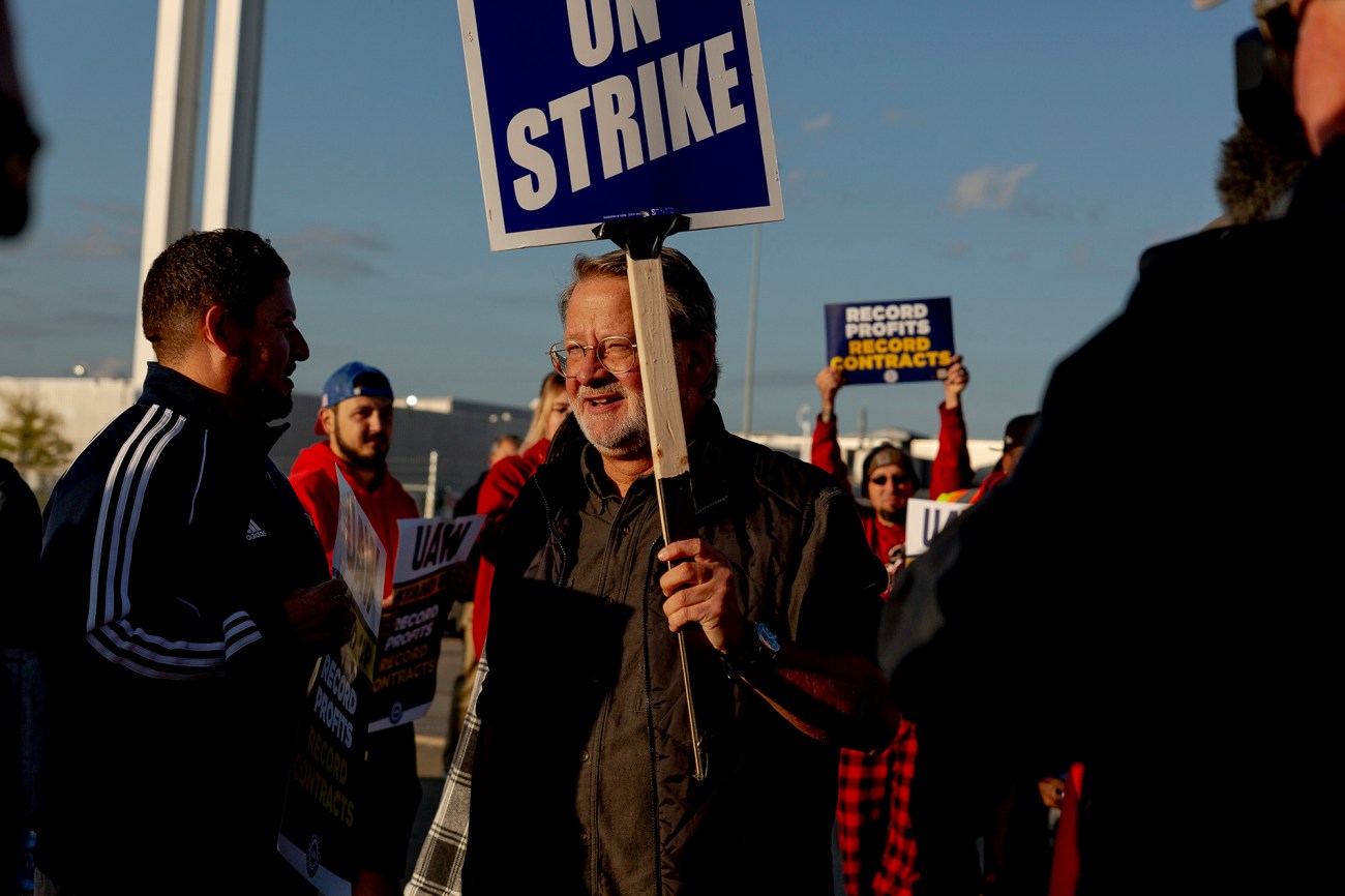 Man holding UAW strike sign while surrounded by people.