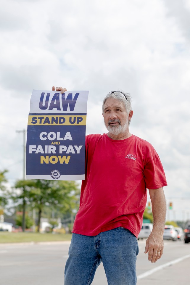 Man in red shirt holding a UAW strike sign.