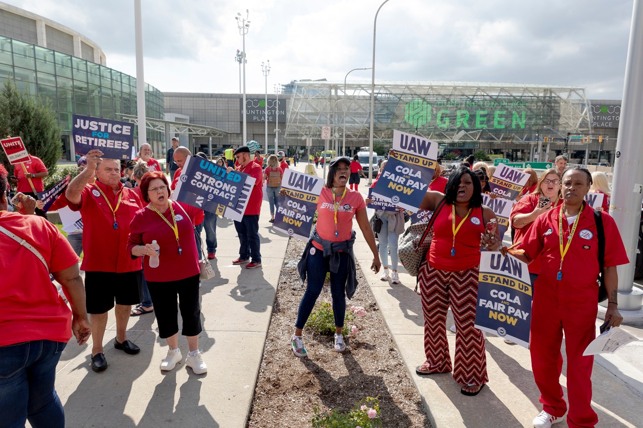 Group of mostly women dressed in red holding UAW strike signs, yelling.