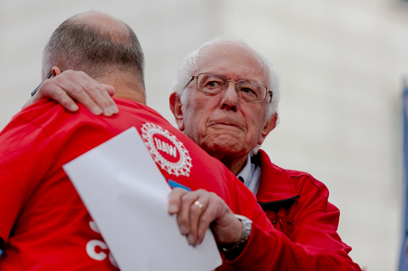 Senator Bernie Sanders hugging a bald man in a red shirt.
