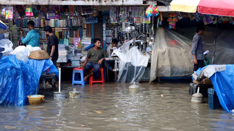 A market experiencing flooding in Bangladesh, with a worker sitting on a chair and people still shopping