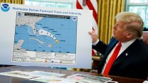 president trump sits in the oval office looking at a chart of a hurricane's path that has been drawn on with a sharpie
