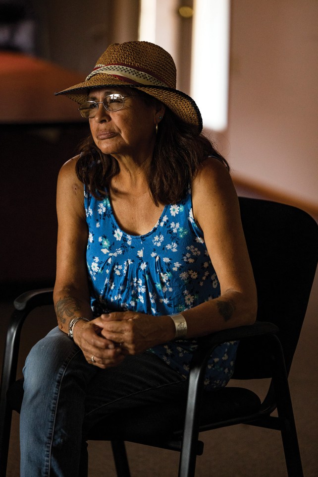 Portrait of woman wearing a blue shirt and a hat, sitting in a chair.