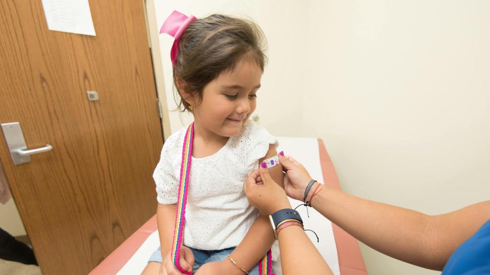 A medical professional putting a bandaid on a young kid after they received a shot or vaccine in a doctor's office