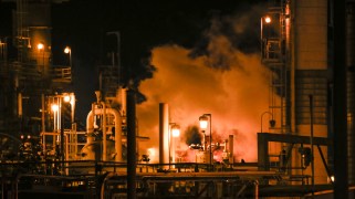 A refinery engulfed in smoke following a fire, at nighttime