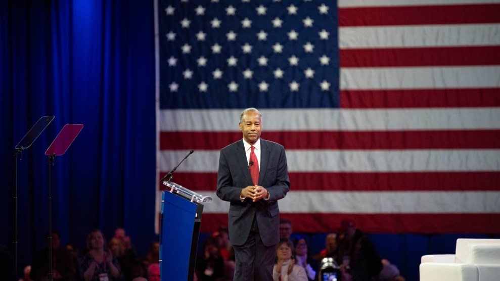 Former HUD secretary Ben Carson stands in front of a large American flag while leaving a podium.