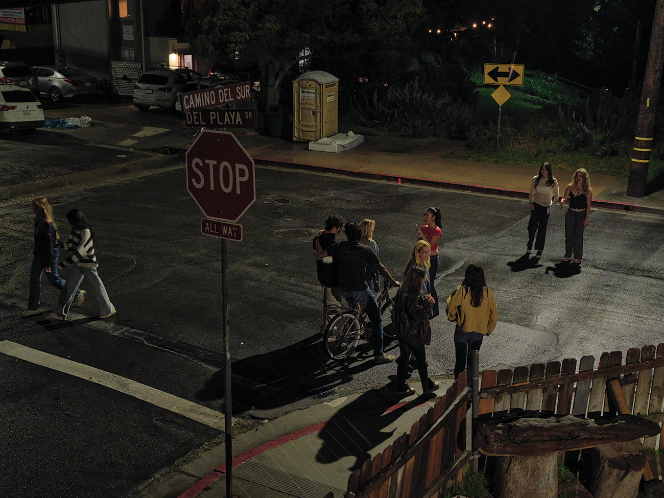 Intersection at night with people standing in the street.