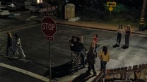 Intersection at night with people standing in the street.
