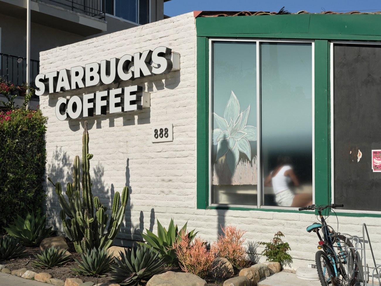 Exterior view of a Starbucks coffee shop with a person leaning against the window inside.