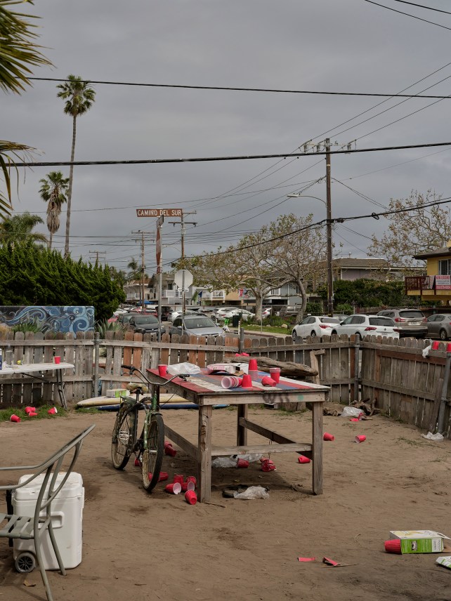 A sandy yard with a wood fence in which a bicycle leans against a wood table with red Solo cups.